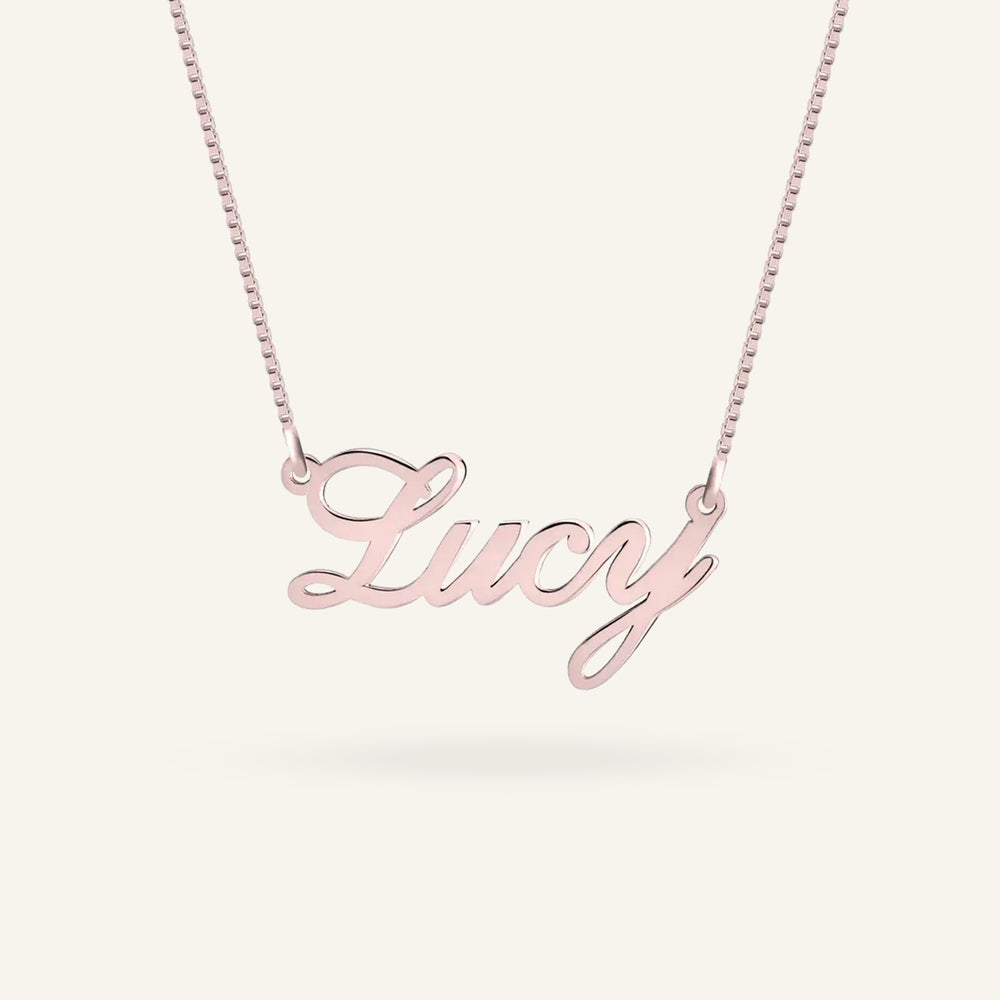 A rose gold script nameplate necklace spelling 'Lucy' on a delicate matching chain, shown against a clean off-white background.